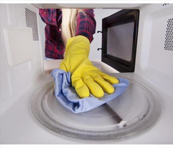 Closeup of hand in protective glove wiping rag microwave. View from the interior of the oven